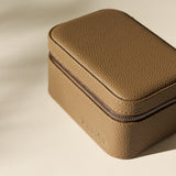 The TAWBURY Fraser 2 Watch Case in taupe, featuring a compact rectangular design and zippered closure, rests on a neutral surface under soft lighting.
