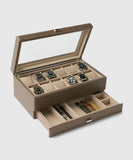 The Bayswater 12 Slot Watch Box with Storage in taupe by TAWBURY is crafted from vegan leather and features a glass lid that elegantly displays up to eight watches. Beneath, a drawer provides space for watch collectors' essentials like straps and tools.