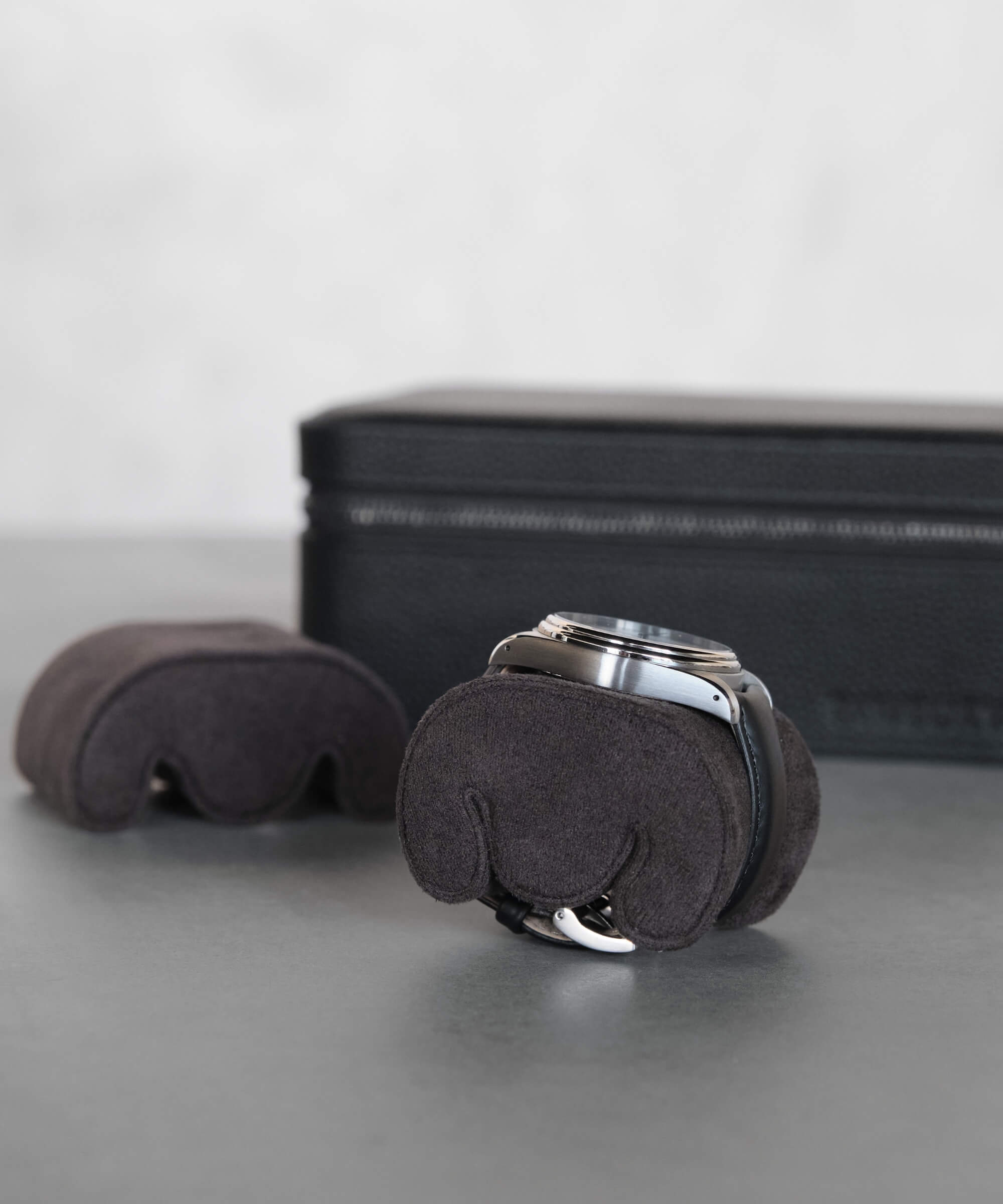 Two Fraser Replacement Watch Case Pillows - X-Small - Black/Charcoal by TAWBURY are encased in protective black covers on a gray surface, with a zippered black case featuring watch slots in the background.