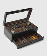 The TAWBURY Bayswater 12 Slot Watch Box in Black/Grey, made from vegan leather, features a transparent lid showcasing six watches on the top layer and includes collector essentials stored in a pull-out drawer beneath.