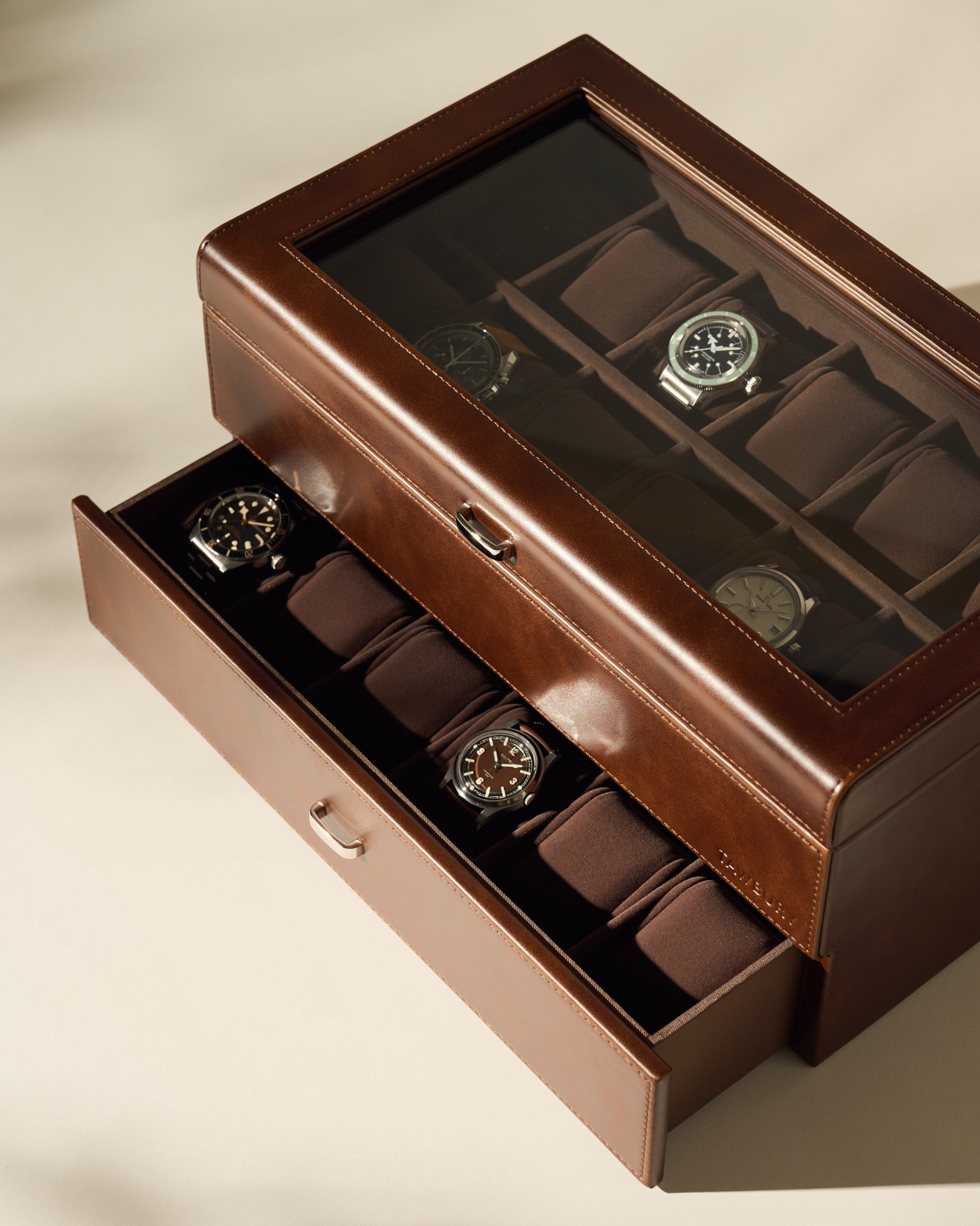 The TAWBURY Bayswater 24 Slot Watch Box with Drawer in brown features a glass lid and two-level padded compartments, offering secure, organized storage for your watch collection.