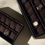 Two TAWBURY Bayswater 24 Slot Watch Boxes with Drawer in Black/Charcoal, each holding wristwatches with some empty slots visible, are displayed on a beige surface.