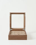The TAWBURY Grove 12 Slot Wooden Watch Box in light walnut features a glass lid and nine beige compartments, shown open on a plain white background.