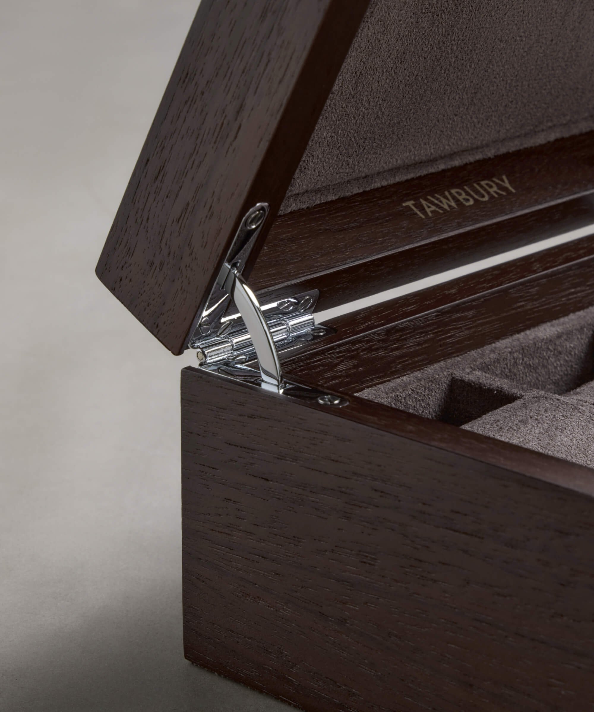Close-up of the TAWBURY Grove 6 Slot Wooden Watch Box in dark walnut with a solid lid, chrome hinge, and soft-lined interior; "TAWBURY" appears inside, making it a refined wooden storage case.