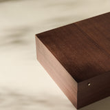 The TAWBURY Grove 12 Slot Wooden Watch Box in dark walnut wood, featuring a solid lid, sits on a light surface with soft shadows highlighting its elegant form.