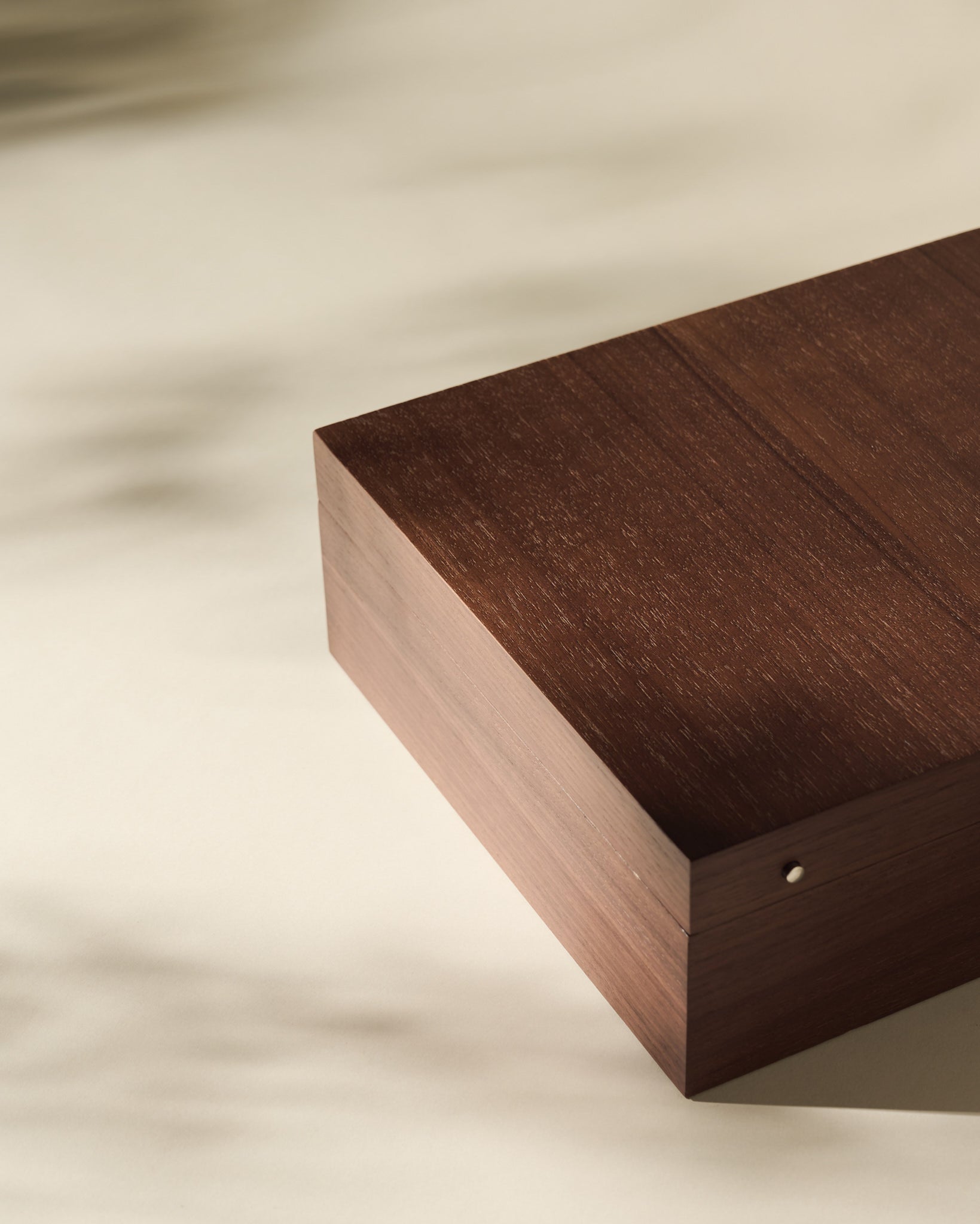 The TAWBURY Grove 12 Slot Wooden Watch Box in dark walnut wood, featuring a solid lid, sits on a light surface with soft shadows highlighting its elegant form.