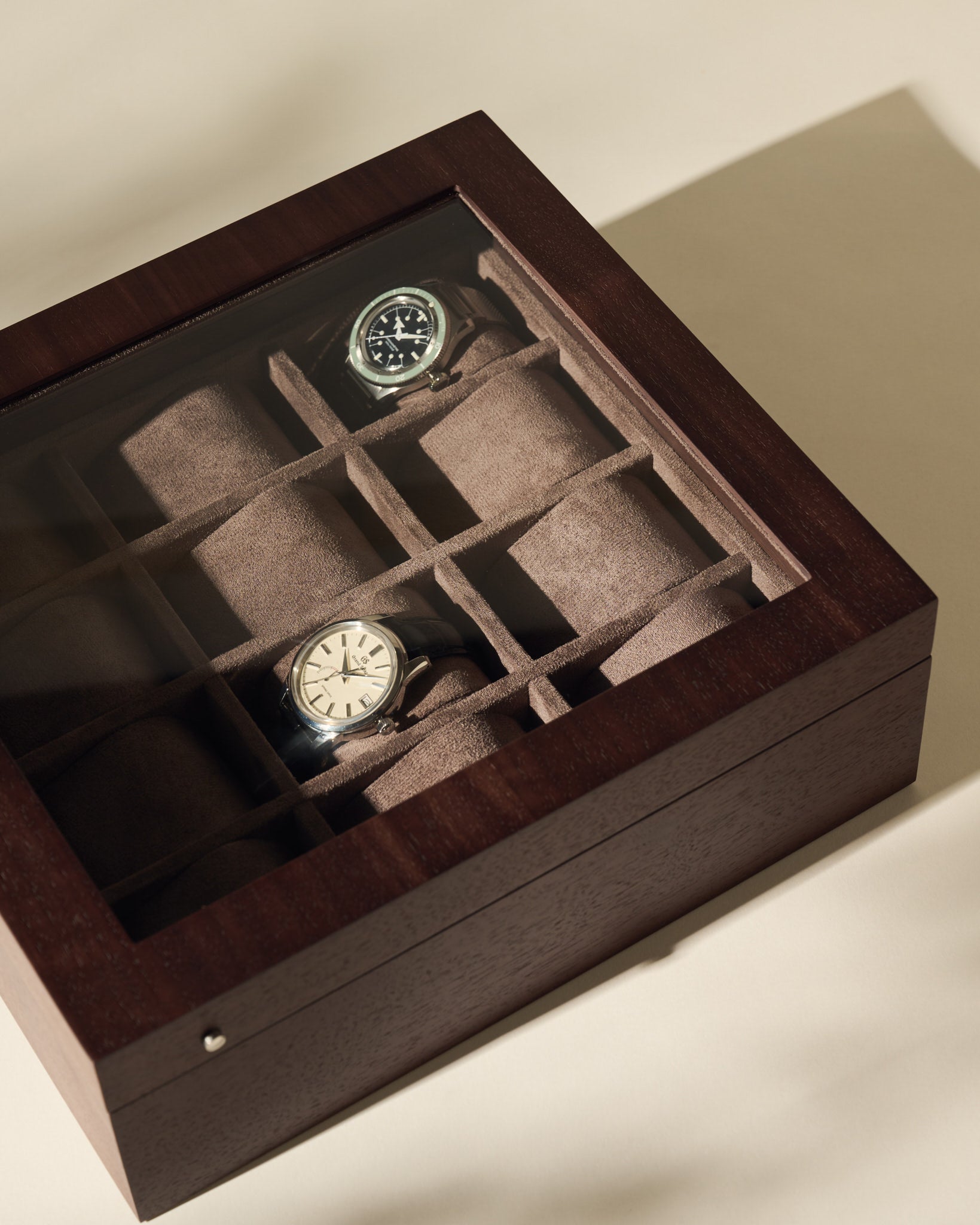 The TAWBURY Grove 12 Slot Wooden Watch Box in dark walnut features a glass lid and individual compartments, making it an elegant storage solution for multiple watches—perfect for collectors.