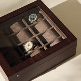 The TAWBURY Grove 12 Slot Wooden Watch Box in dark walnut features a glass lid and individual compartments, making it an elegant storage solution for multiple watches—perfect for collectors.