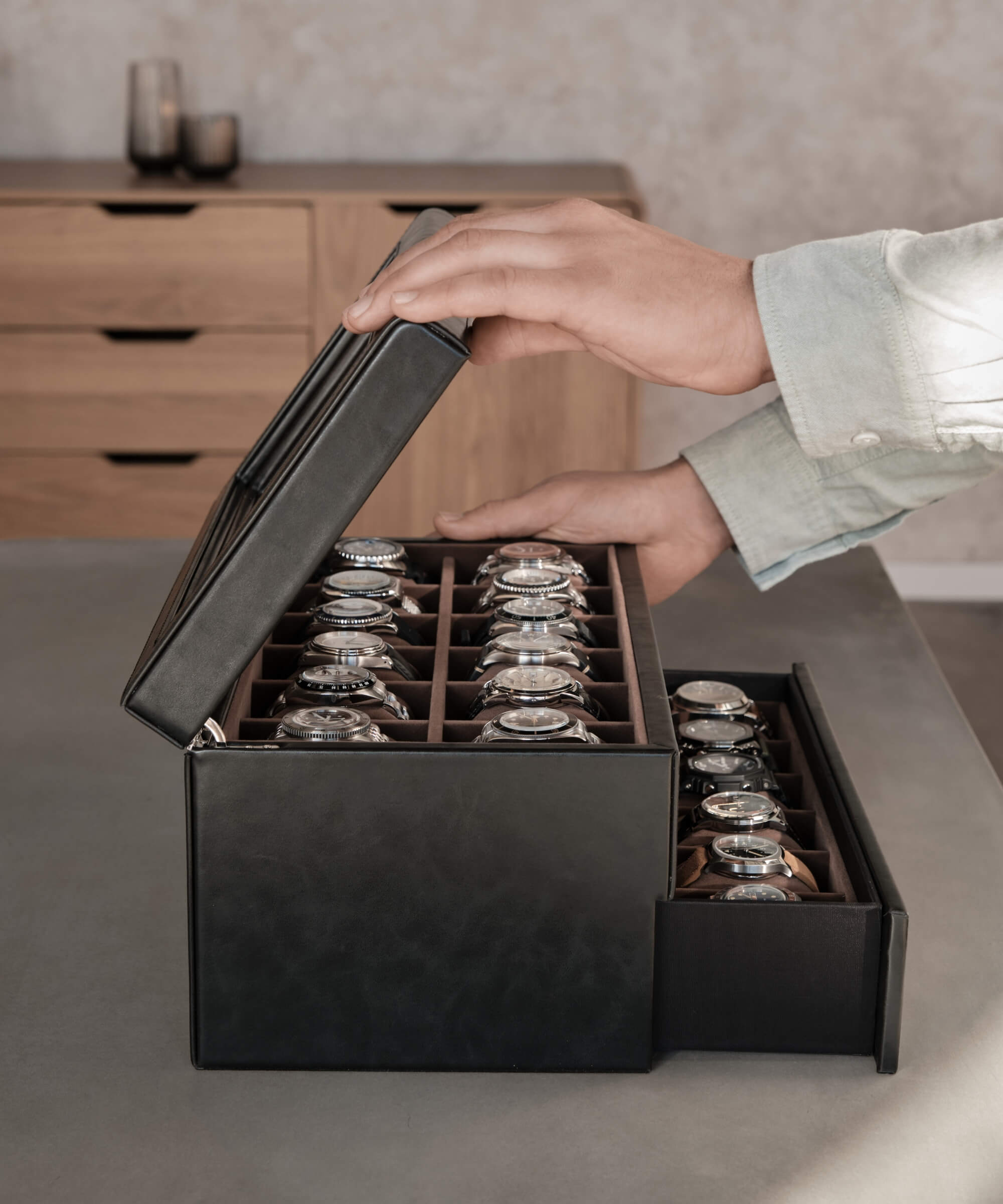 A person is opening a TAWBURY Bayswater 24 Slot Watch Box with Drawer - Black to organize their timepieces on a table.