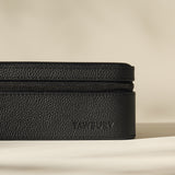 A black textured rectangular leather Fraser 3 Watch Case by TAWBURY, featuring a zippered closure and "TAWBURY" embossed on the side, placed on a plain light surface with a neutral background.
