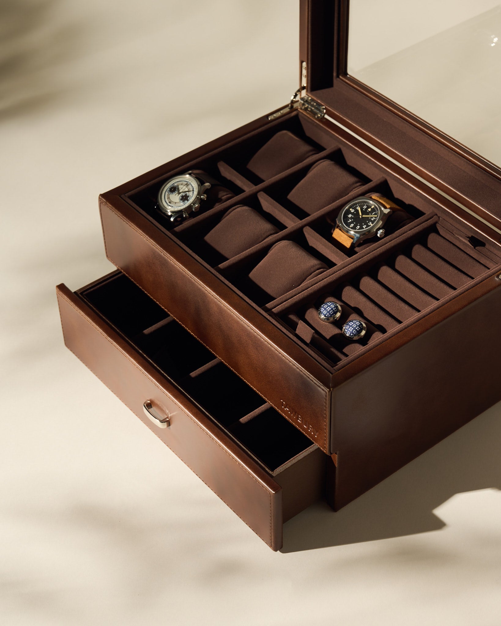 The TAWBURY Bayswater 6 Watch Jewelry Box in brown is shown with its lid open, displaying two wristwatches, two pairs of cufflinks, empty compartments, and a partially open lower drawer.