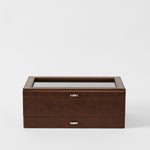 The TAWBURY Bayswater 12 Slot Watch Box with Storage in Chestnut Brown features a glass top and metal handle, ideal for storing and displaying watches, shown against a plain white background.