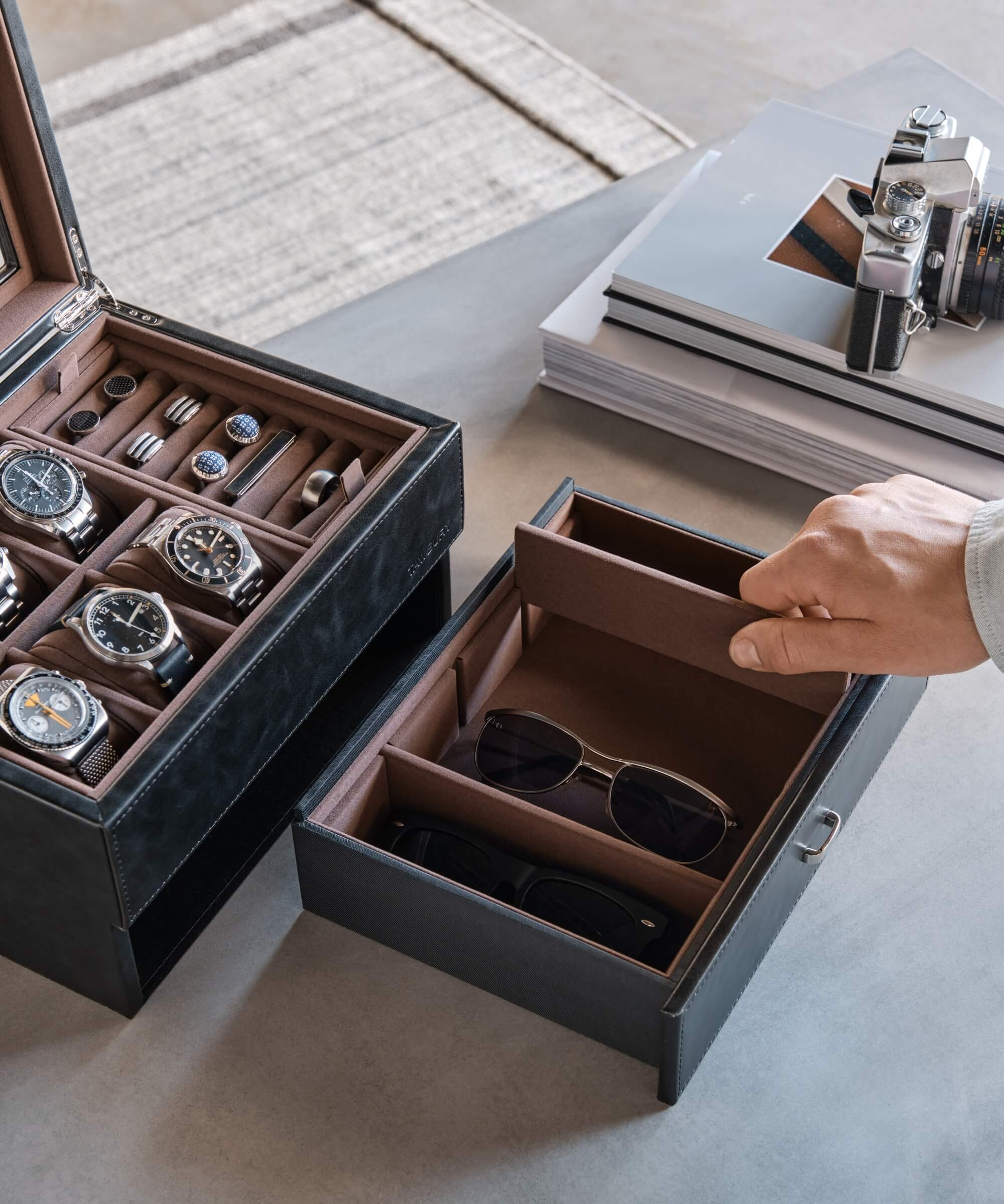A person is opening a TAWBURY Bayswater 6 Watch Jewellery Box - Black to organise and protect their watches on a table.