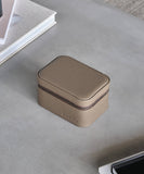 The TAWBURY Fraser 2 Watch Travel Case - Taupe, a tan leather case perfect for watch lovers, is sitting on a table next to a phone. It provides excellent protection while traveling.
