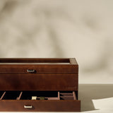 The TAWBURY Bayswater 12 Slot Watch Box with Storage in brown, featuring organized compartments and a partially open drawer, is displayed on a neutral background.