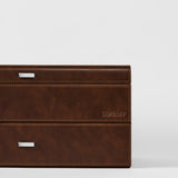 A close-up of the TAWBURY Bayswater 24 Slot Watch Box with Drawer in brown leather, featuring metal handles and “TAWBURY” embossed on the side, set against a plain white background.