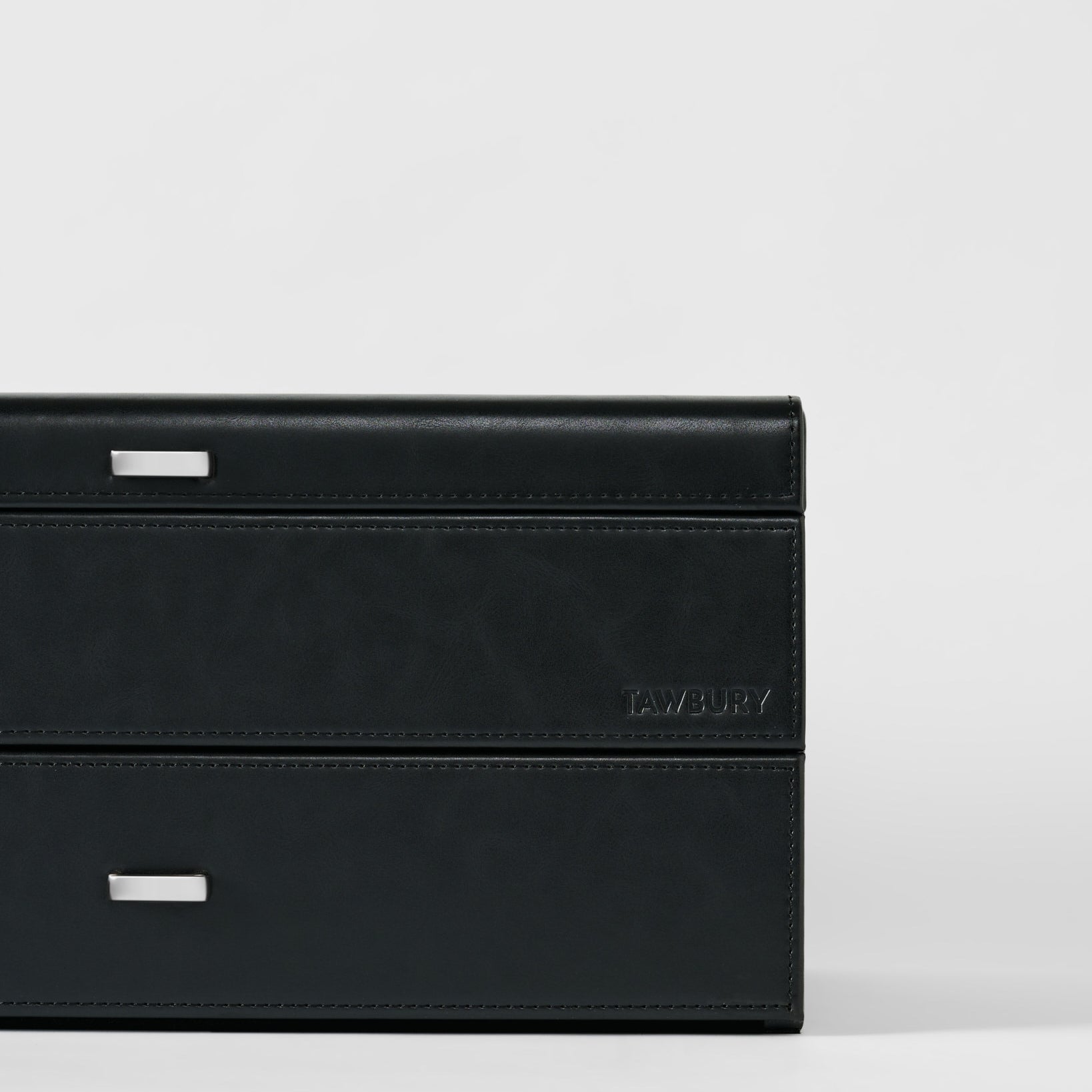 The Bayswater 24 Slot Watch Box with Drawer in black/charcoal by TAWBURY features silver handles and an embossed brand name, offering stylish watch storage, shown on a plain white background.