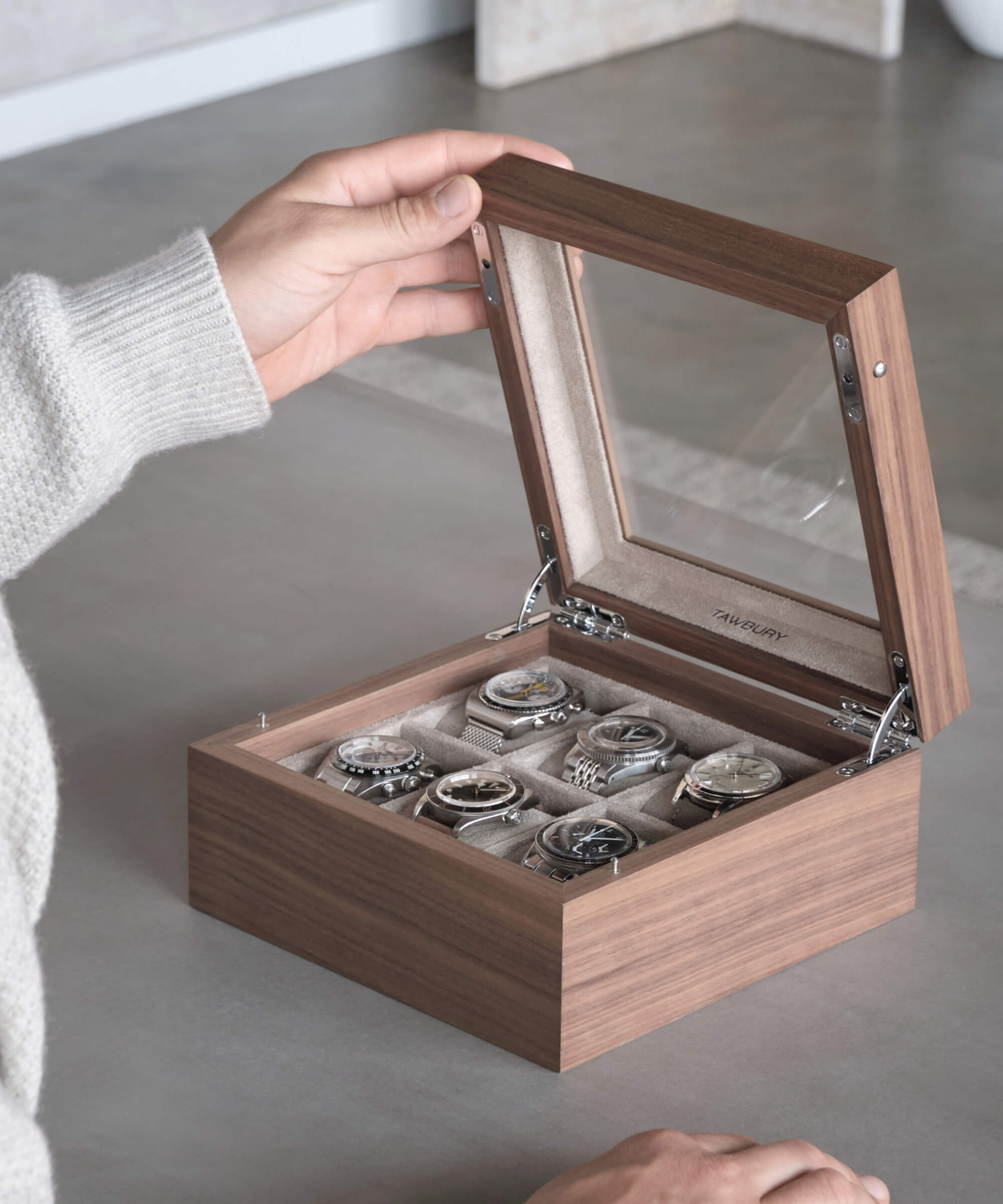 A person is opening a TAWBURY Grove 6 Slot Watch Box with Glass Lid - Walnut containing their cherished timepieces.
