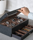 A man is holding a TAWBURY Bayswater 12 Slot Watch Box with Drawer in black, used for storage.