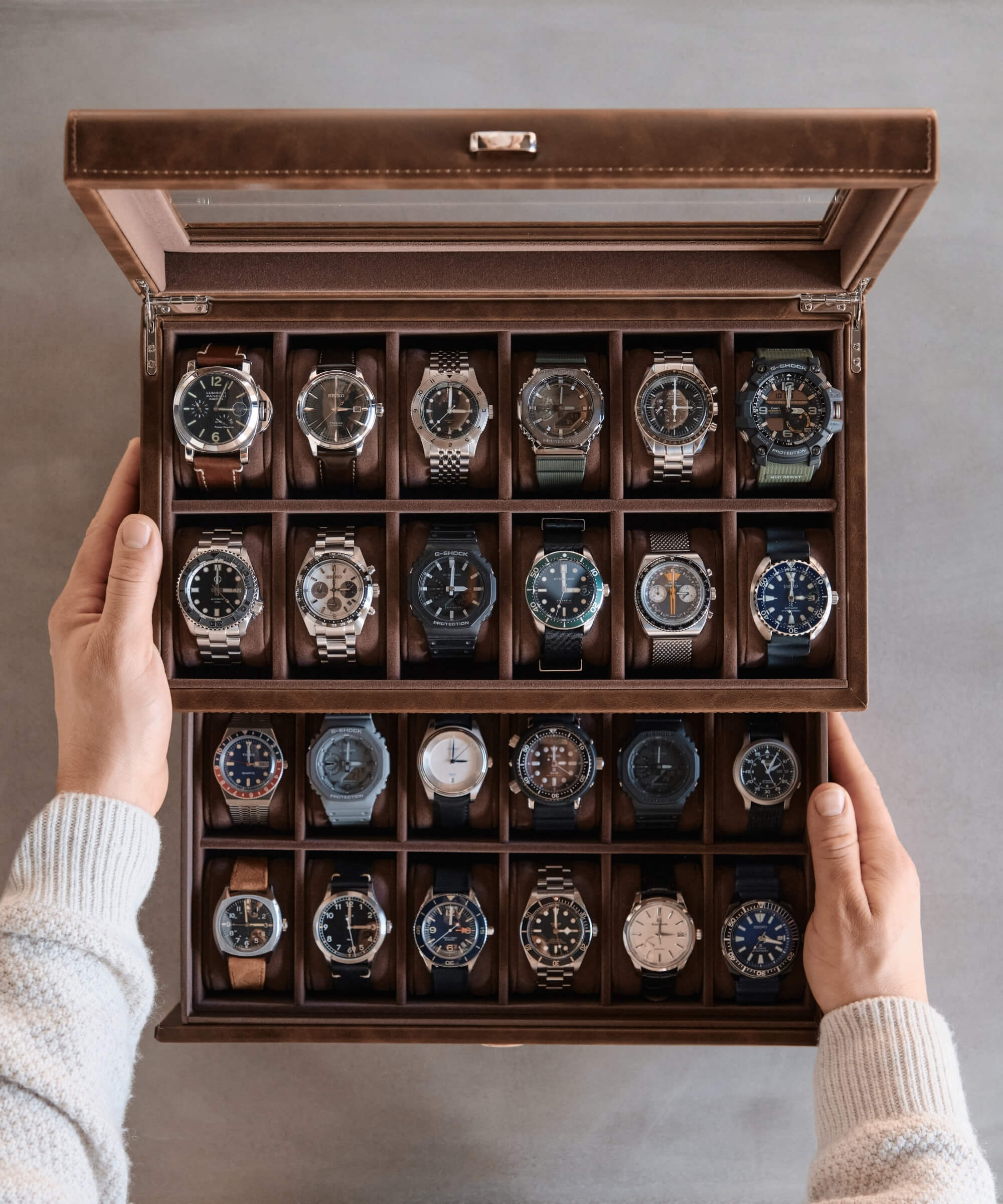 A watch enthusiast holding a TAWBURY Bayswater 24 Slot Watch Box with Drawer - Brown filled with timepieces.