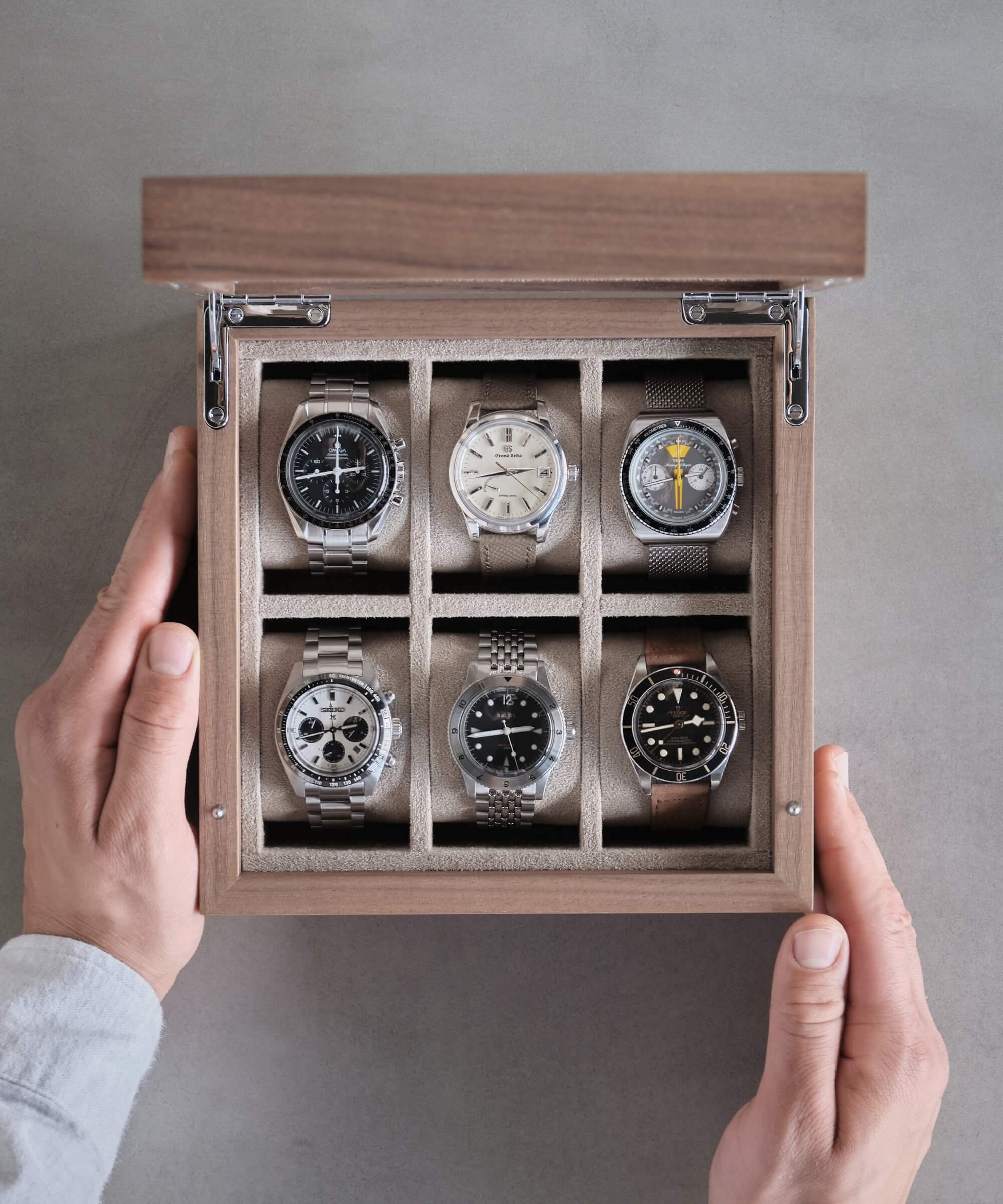 A watch enthusiast holding a TAWBURY Grove 6 Slot Watch Box with Glass Lid - Walnut.