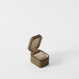 The TAWBURY Fraser 1 Watch Case in Truffle Taupe is a compact, square, textured brown leather case with a hinged lid, open to reveal its beige padded interior against a plain white background.