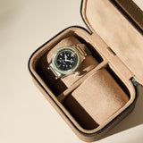 A wristwatch with a black face and metal strap is displayed inside the open TAWBURY Fraser 2 Watch Case in taupe.