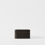 The Fraser 4 Watch Case by TAWBURY is a compact, rectangular espresso brown textured leather case with a zipper and "TAWBURY" embossed on the front, ideal for storing four watches. Shown on a plain white background.
