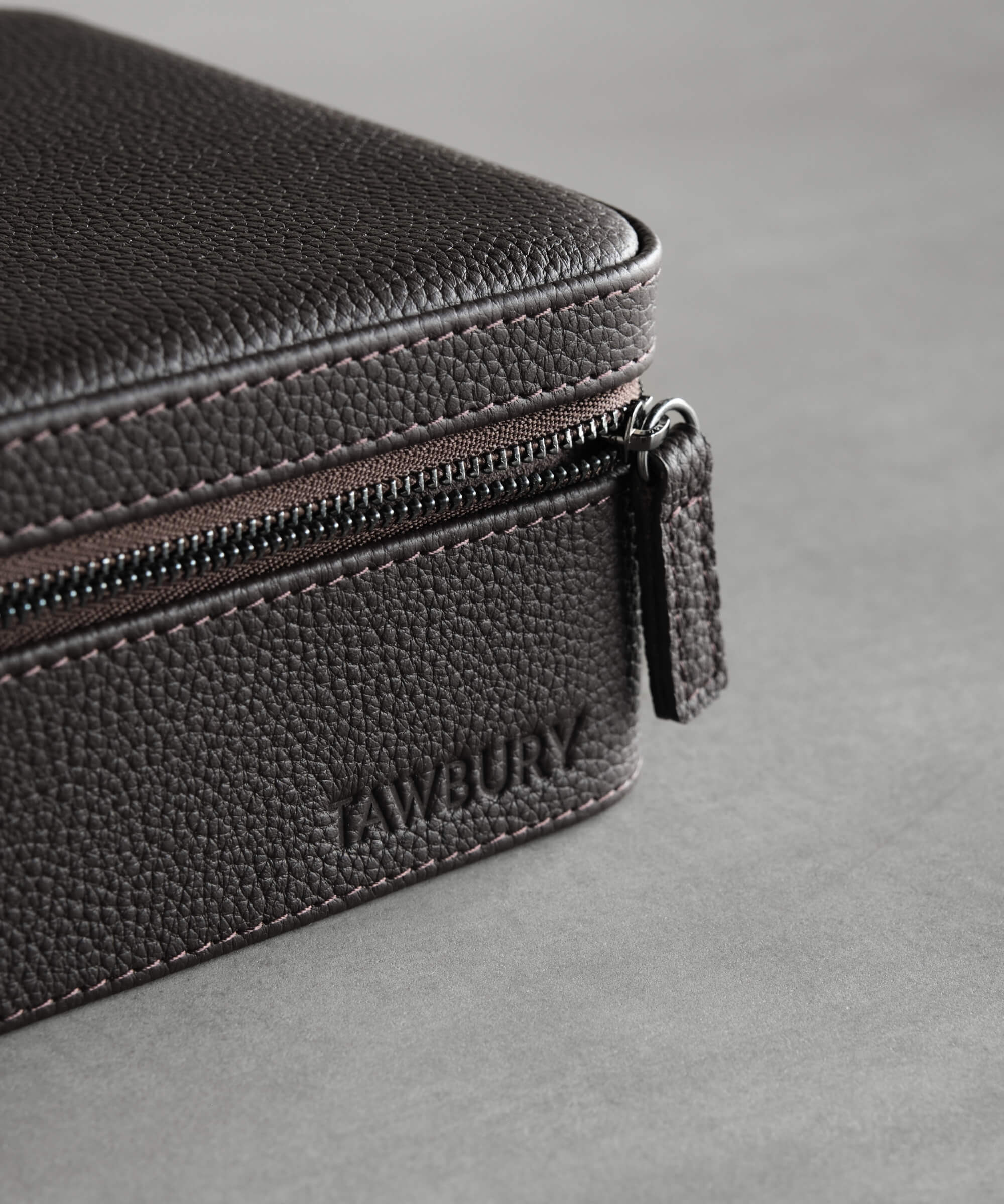A close-up of a textured brown leather pouch with a zipper and the word "TAWBURY" embossed on it, reminiscent of the refined design seen in the Fraser 6 Watch Travel Case - Brown (Coming Soon).