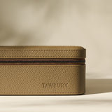 A close-up of the textured, taupe-colored Fraser 6 Watch Case by TAWBURY with the brand name embossed on the side, set against a neutral background.