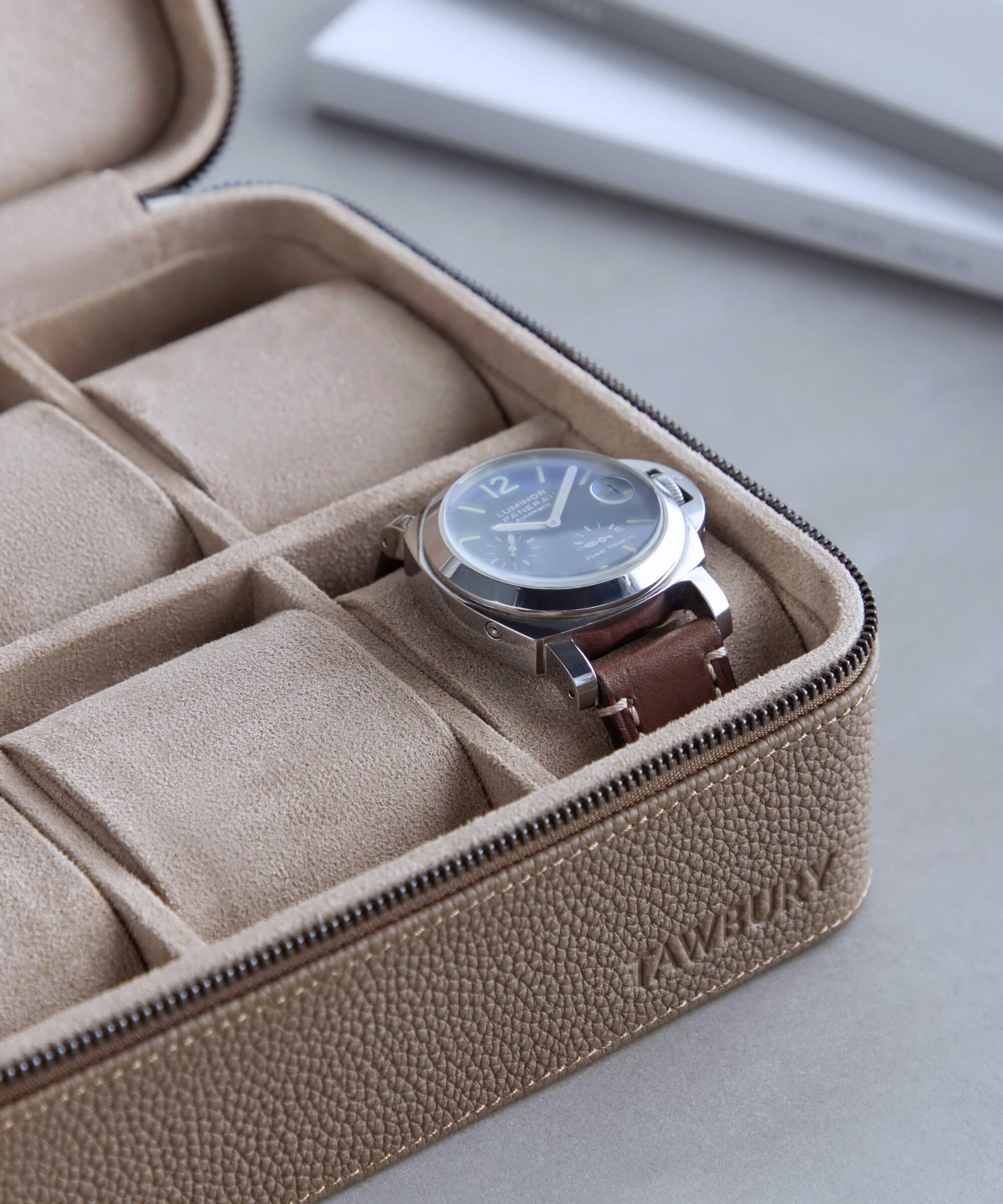 A wristwatch with a brown leather strap nestled in the TAWBURY Fraser 6 Watch Travel Case - Taupe, featuring beige zippered compartments for optimal watch storage.