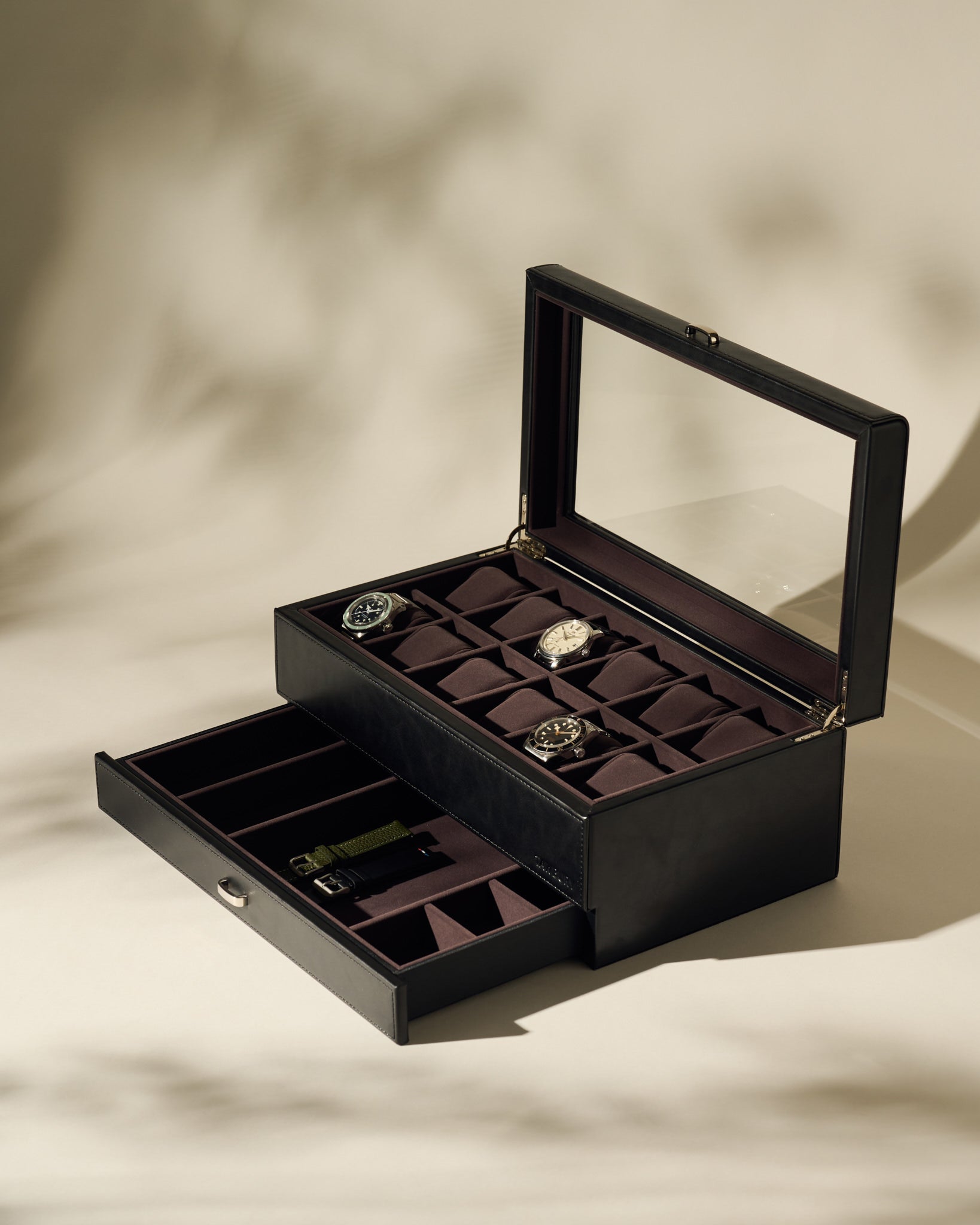 The TAWBURY Bayswater 12 Slot Watch Box with Storage in Black/Charcoal features a glass lid and organizes multiple watches and accessories neatly in compartments, displayed on a neutral surface.