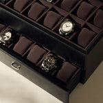 The TAWBURY Bayswater 24 Slot Watch Box with Drawer in Black/Charcoal is partially open, revealing two layers of neatly arranged watches and some empty spaces, ideal for displaying an impressive collection.