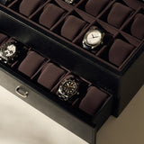 The TAWBURY Bayswater 24 Slot Watch Box with Drawer in Black/Charcoal is partially open, revealing two layers of neatly arranged watches and some empty spaces, ideal for displaying an impressive collection.