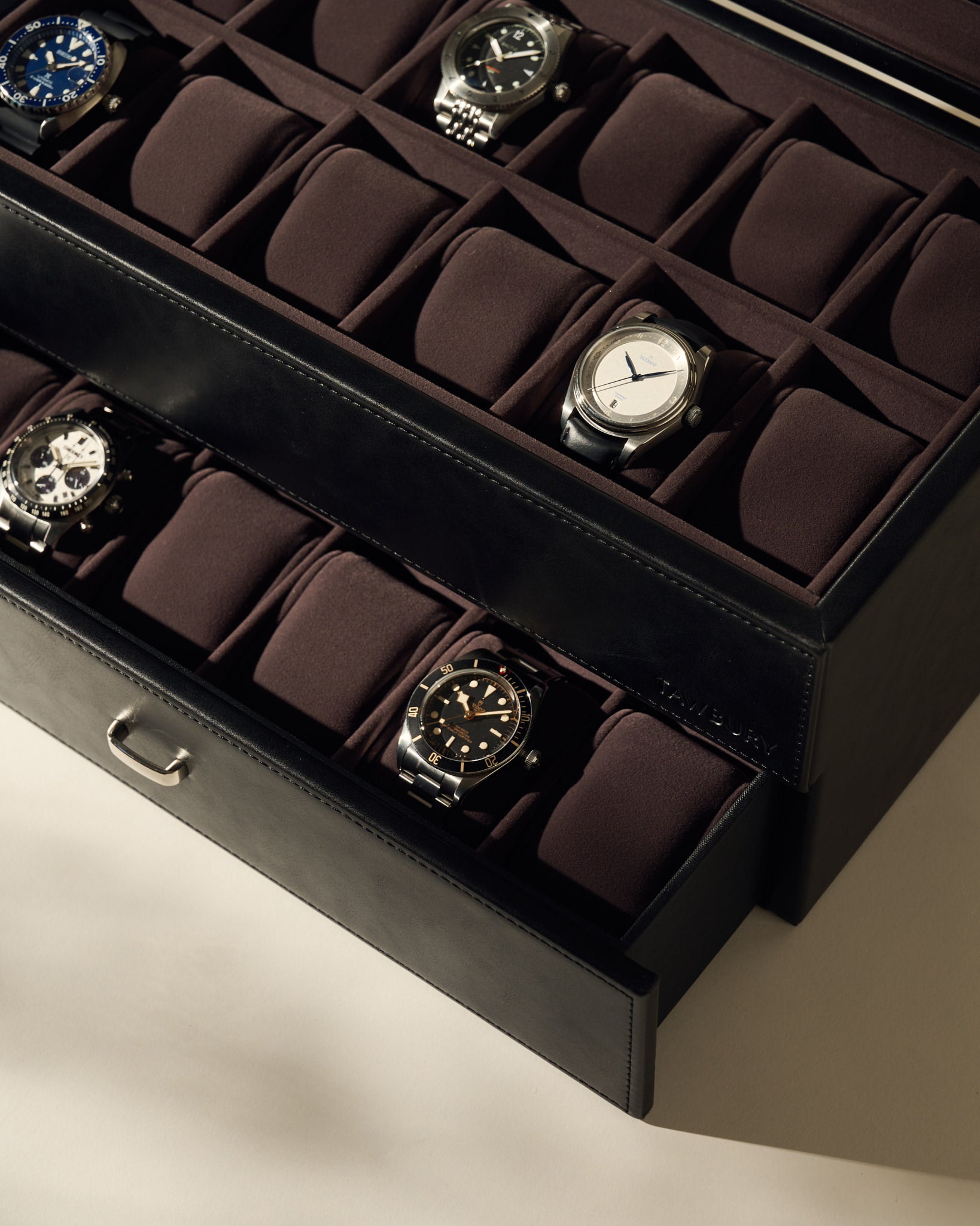 The TAWBURY Bayswater 24 Slot Watch Box with Drawer in Black/Charcoal is partially open, revealing two layers of neatly arranged watches and some empty spaces, ideal for displaying an impressive collection.