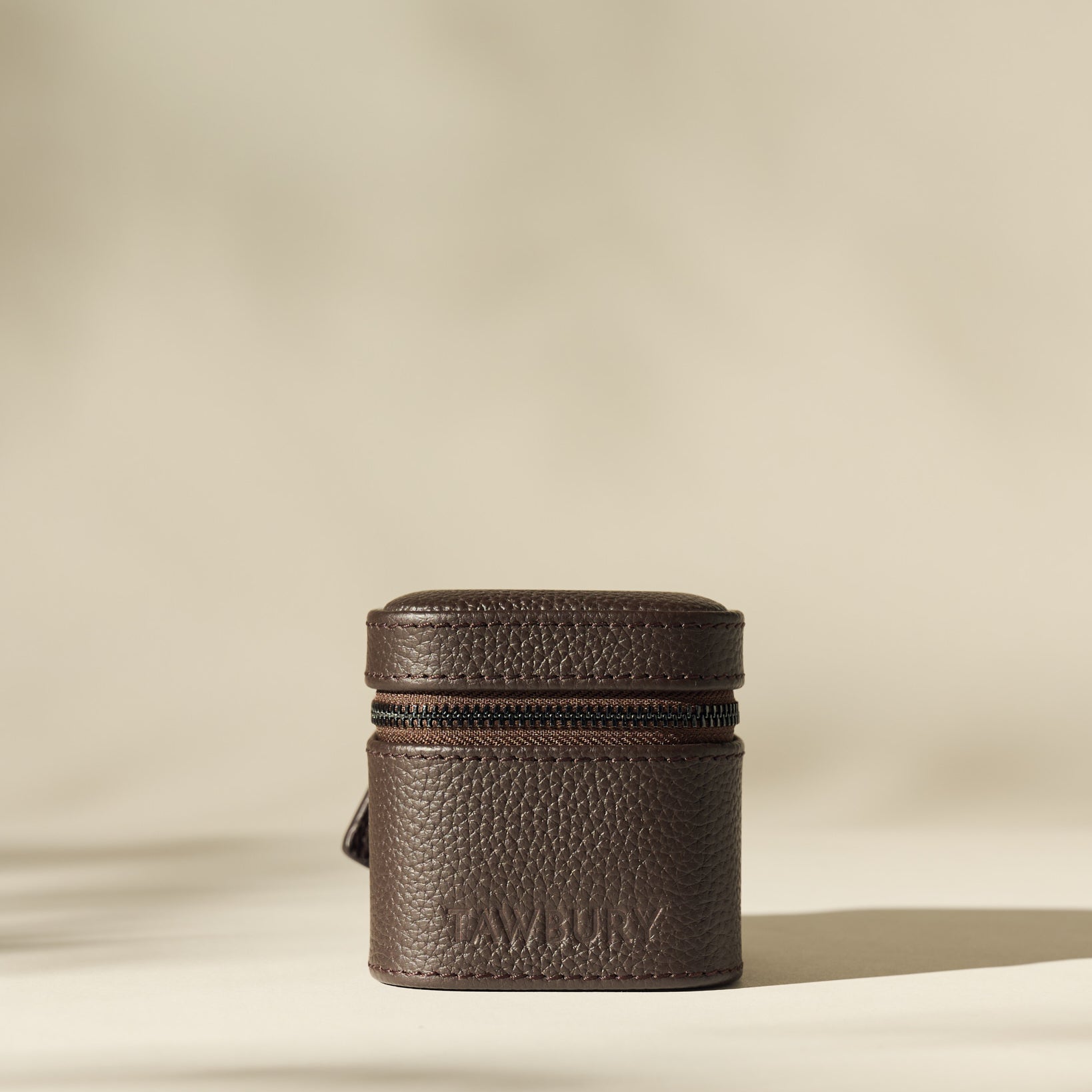 The TAWBURY Fraser 1 Watch Case in rich brown leather stands upright on a neutral surface with soft lighting and a blurred beige background—ideal for stylish travel watch storage.