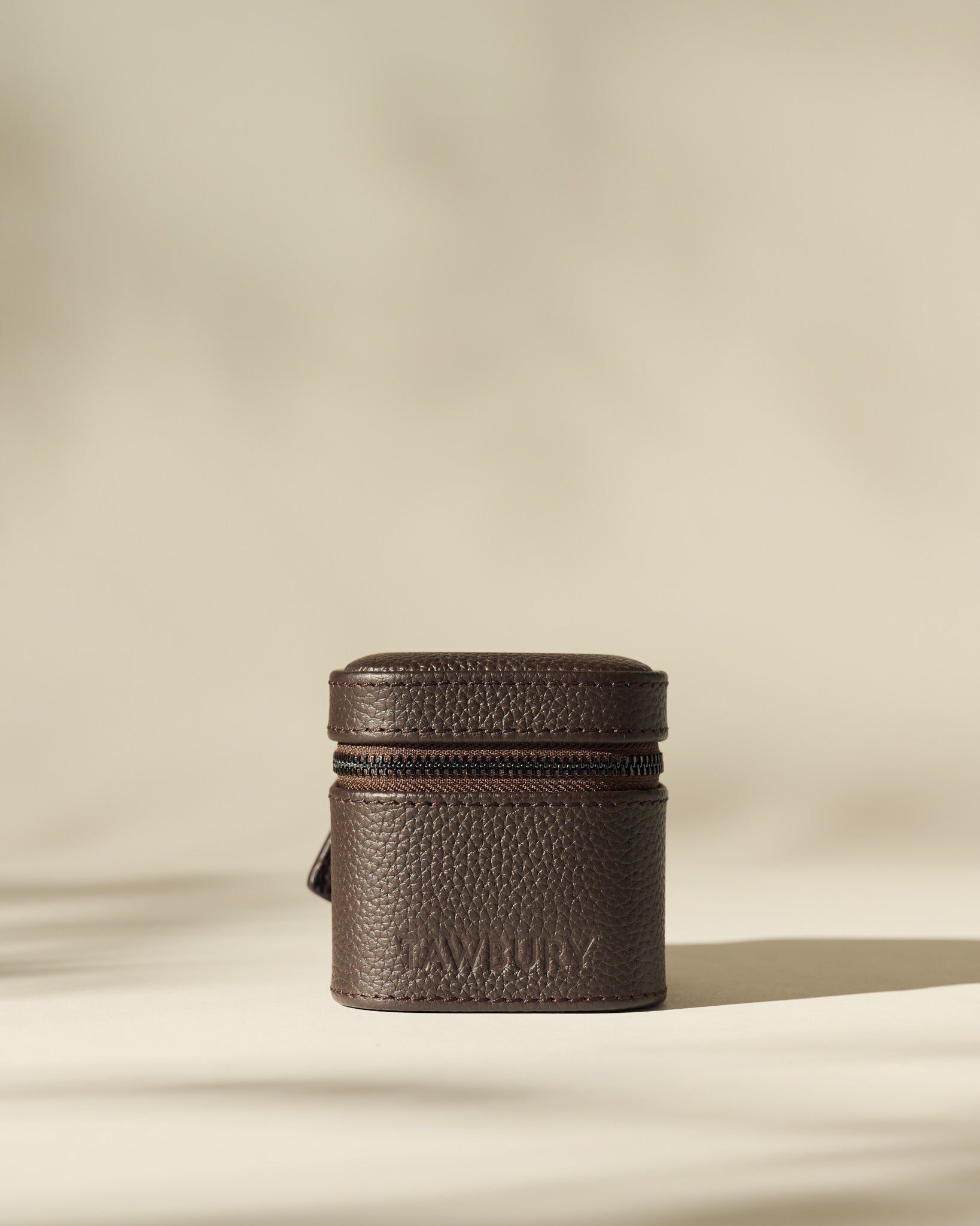 The TAWBURY Fraser 1 Watch Case in rich brown leather stands upright on a neutral surface with soft lighting and a blurred beige background—ideal for stylish travel watch storage.
