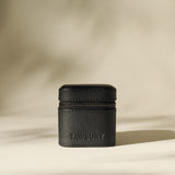 A small, black Fraser 1 Watch Case by TAWBURY stands upright on a neutral background, featuring a textured leather finish and the brand name on the front.