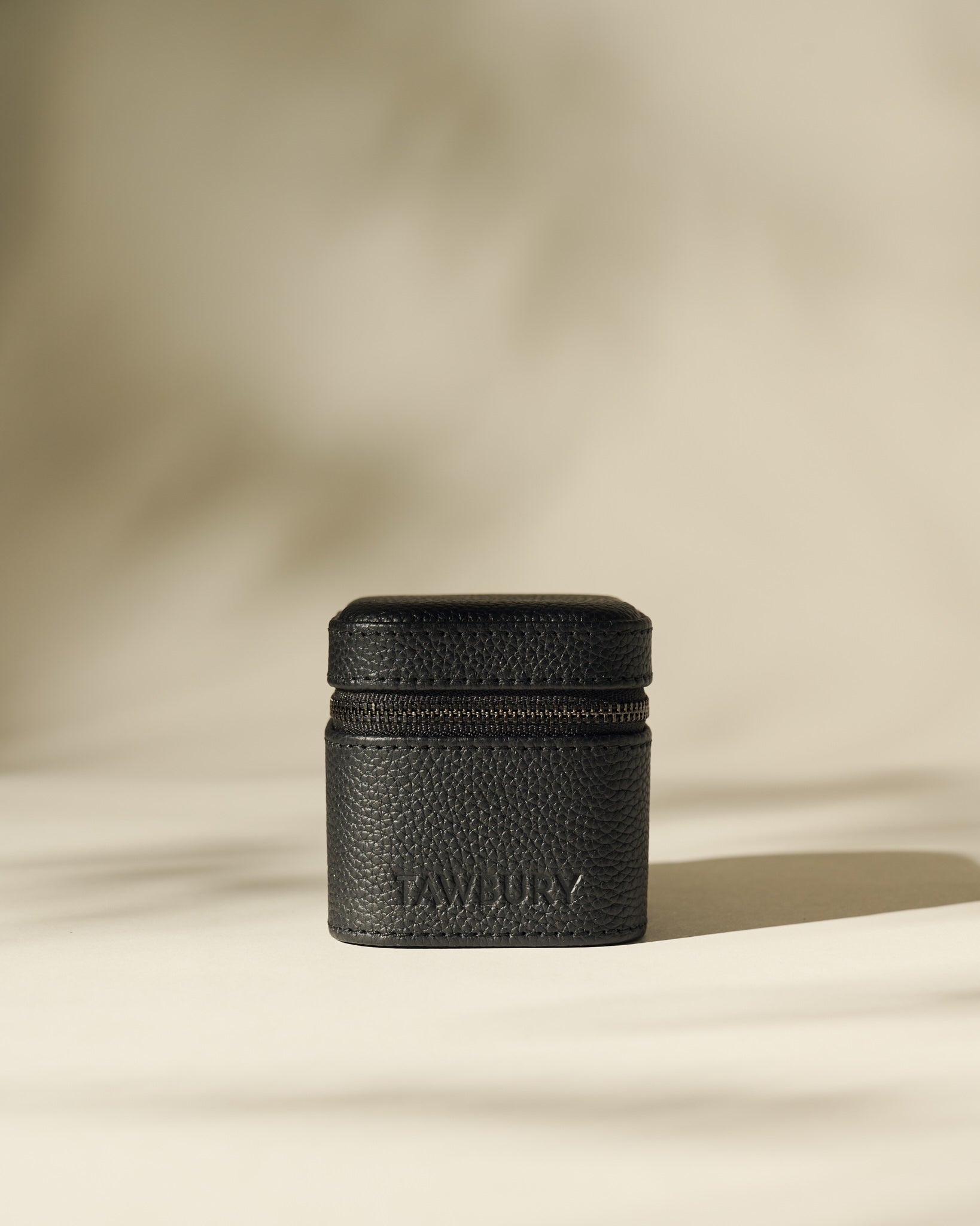 A small, black Fraser 1 Watch Case by TAWBURY stands upright on a neutral background, featuring a textured leather finish and the brand name on the front.