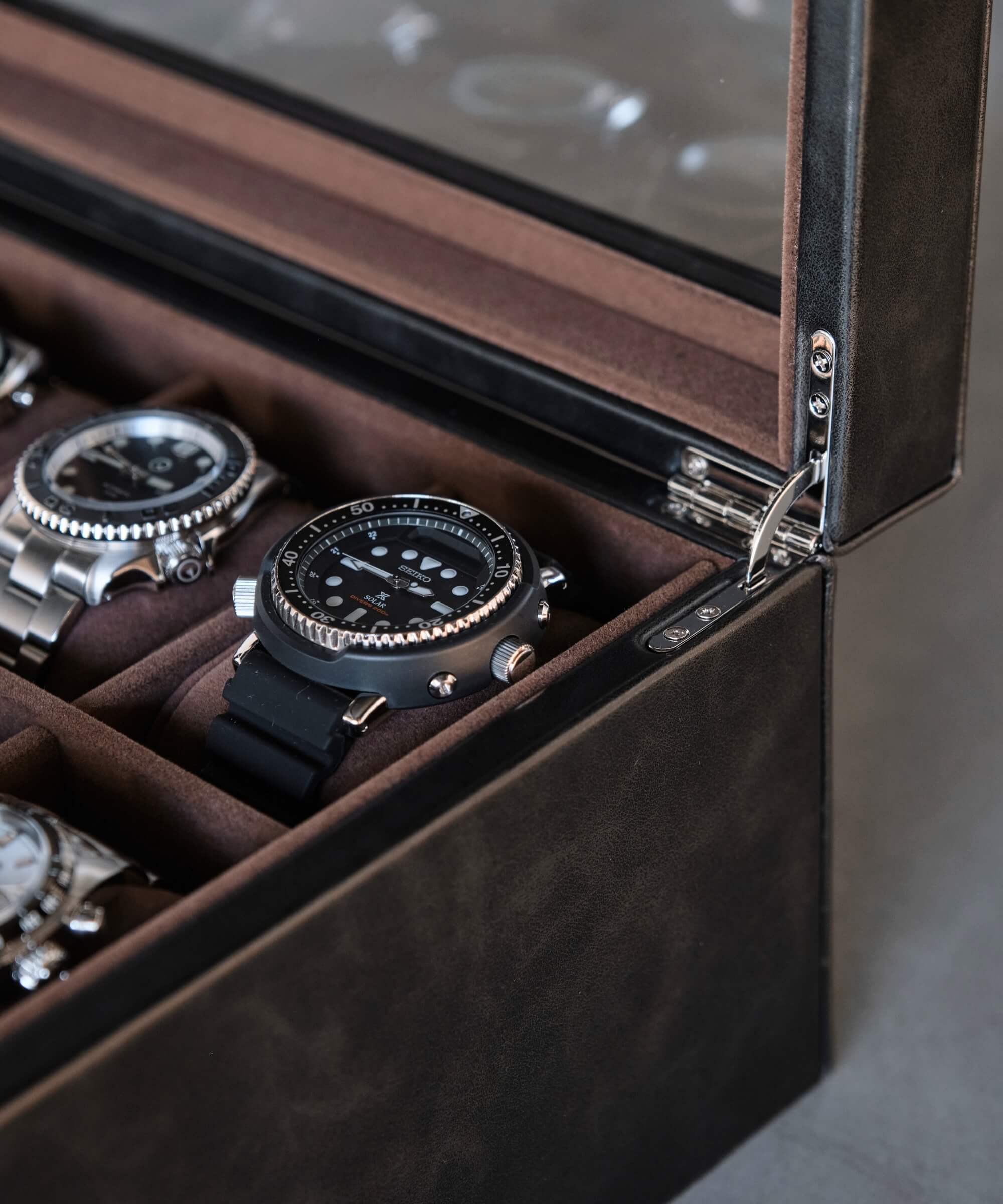A TAWBURY Bayswater 12 Slot Watch Box with Drawer - Black filled with an assortment of timepieces.
