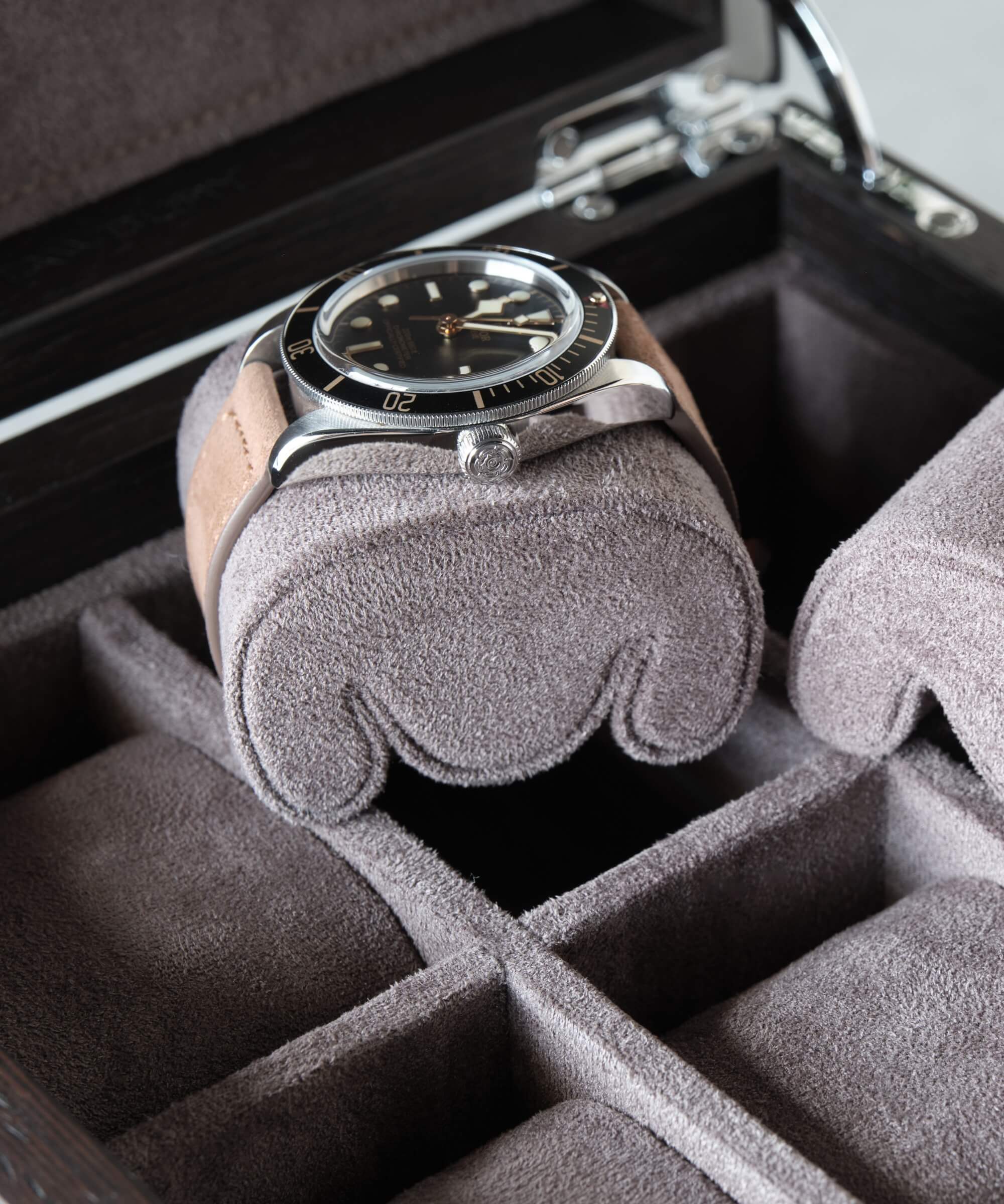 A wristwatch with a black dial and brown strap is placed on a slender wrist pillow inside one of the watch slots in a Grove Replacement Watch Box Pillows - X-Small - Brown/Grey by TAWBURY.