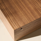 Close-up of the TAWBURY Grove 12 Slot Wooden Watch Box in Light Walnut Wood with a solid lid, featuring a small round hole on the side, photographed on a light-colored surface.