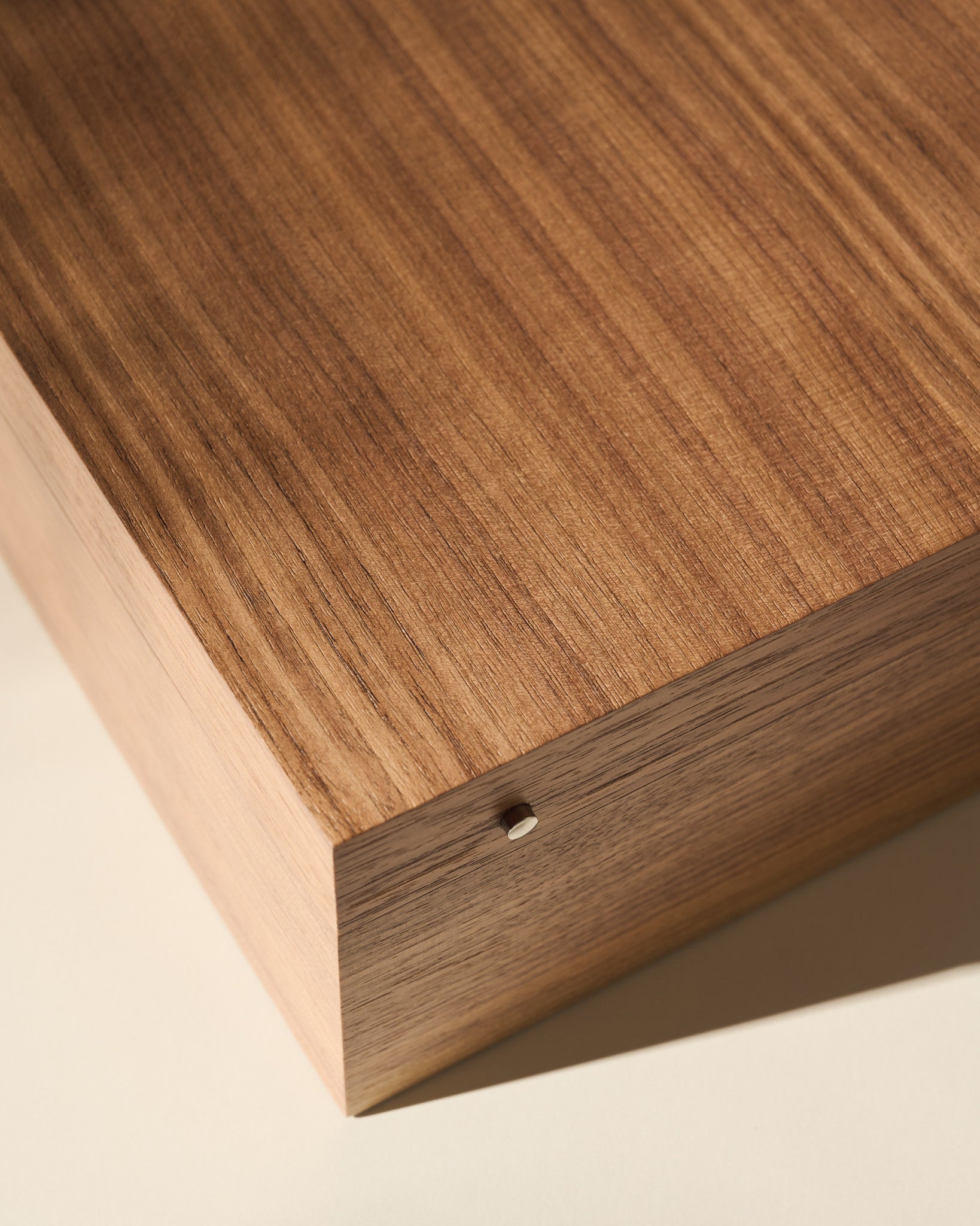 Close-up of the TAWBURY Grove 12 Slot Wooden Watch Box in Light Walnut Wood with a solid lid, featuring a small round hole on the side, photographed on a light-colored surface.