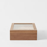 The TAWBURY Grove 12 Slot Wooden Watch Box in classic walnut wood features a glass lid and divided compartments, displayed against a plain white background.