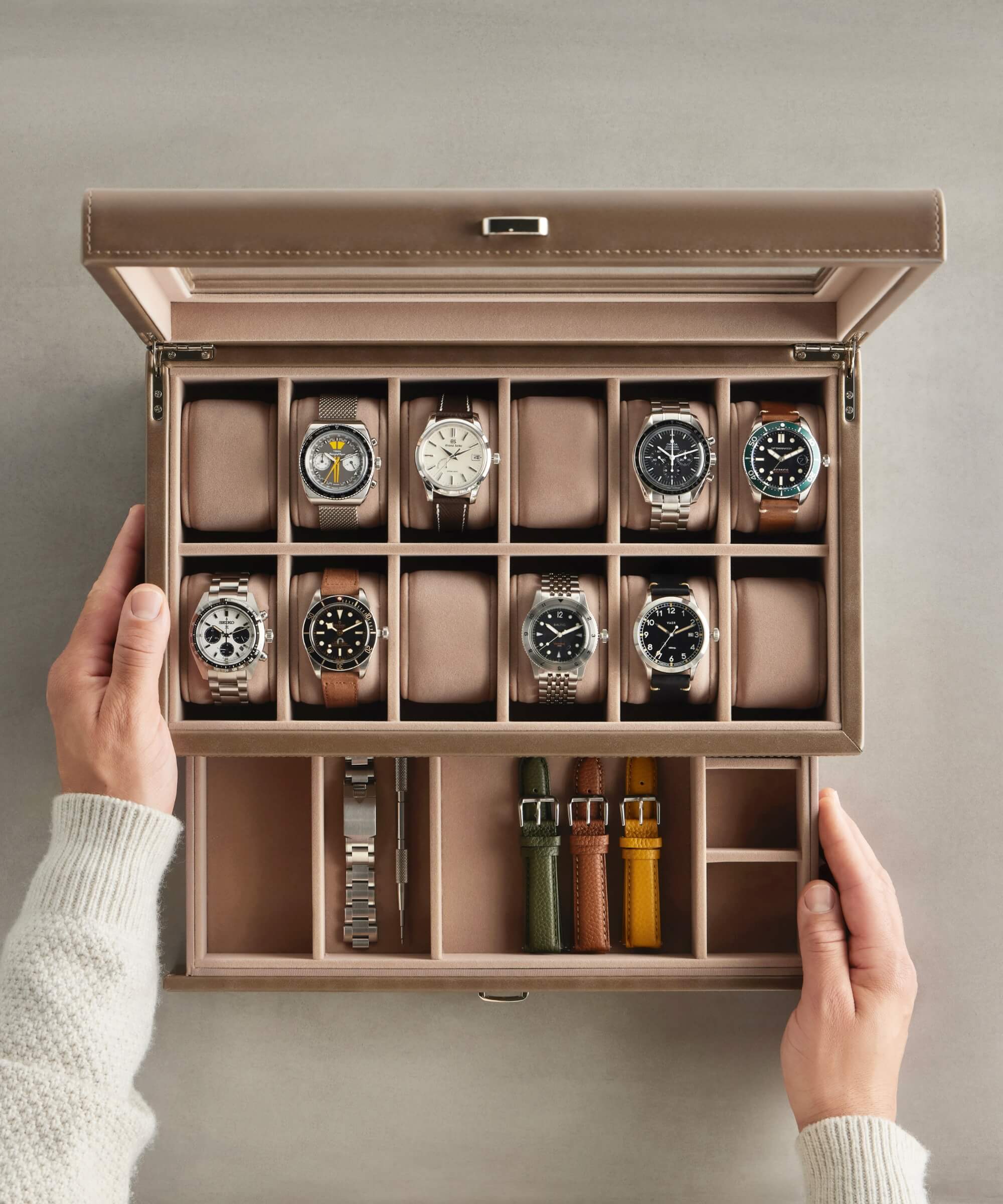 A watch collector's dream, the Bayswater 12 Slot Watch Box with Storage in Taupe by TAWBURY elegantly displays up to twelve exquisite timepieces, with additional compartments for four spare straps, all meticulously organized.