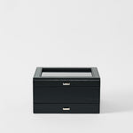 The TAWBURY Bayswater 8 Slot Watch Box with Storage in Midnight Black features a glass top and two metal handles, offering elegant watch storage, showcased against a plain white background.