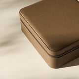 The TAWBURY Fraser 6 Watch Case in taupe features a square, textured leather design with a zipper, shown on a light surface with soft shadows.