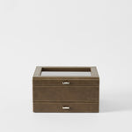 The Bayswater 8 Slot Watch Box with Storage in Driftwood Taupe by TAWBURY features a glass top, metal drawer handle, and "TAWBURY" embossed on the front—perfect for elegant watch storage against a plain white background.