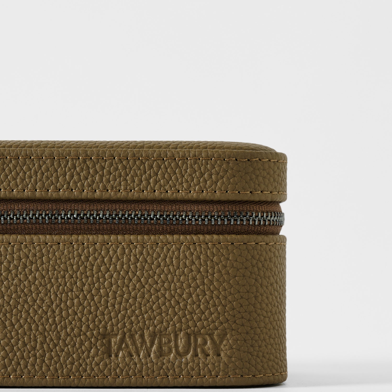 A close-up of the textured taupe leather Fraser 3 Watch Case with the brand name "TAWBURY" embossed on the lower front.