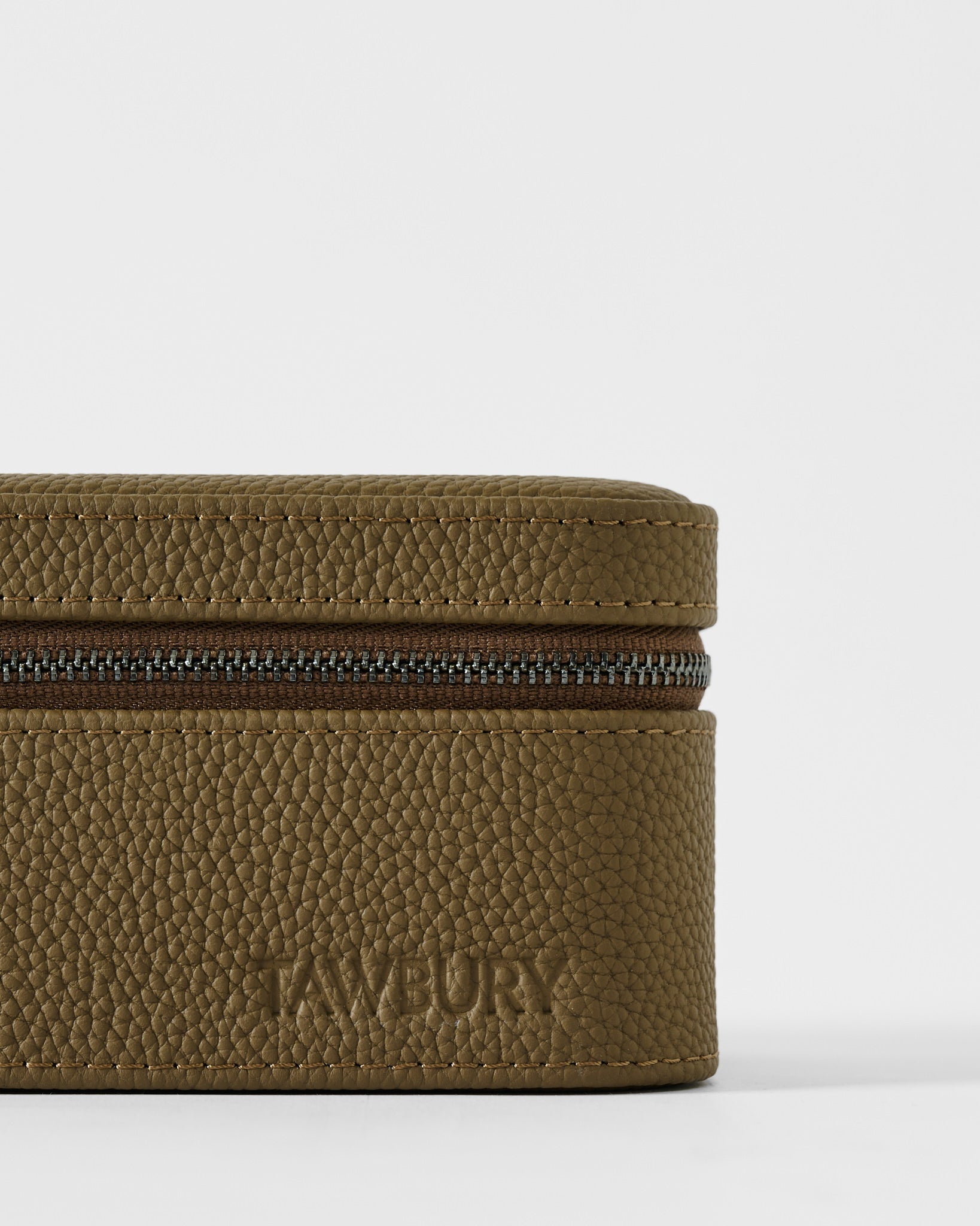 A close-up of the textured taupe leather Fraser 3 Watch Case with the brand name "TAWBURY" embossed on the lower front.